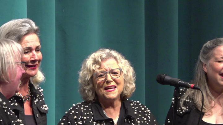Green curtain background. A quartet of ladies in black and gold singing.