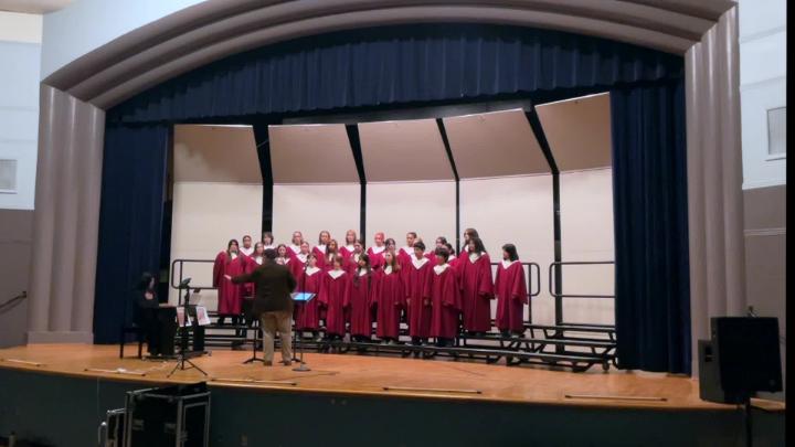 Students dressed in red on a stage singing.