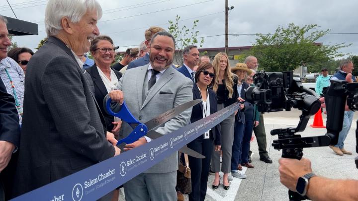 A group of well dressed individuals outside using giant scissors to cut a ribbon