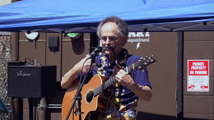 Man in a purple shirt playing guitar outside