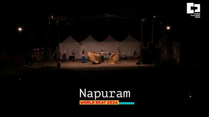 Dancers on a dark stage with white words at the bottom: Nupuram