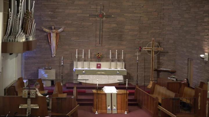 Church sanctuary with brick walls, an altar and candles in the center and a statue of Jesus on the cross to the left